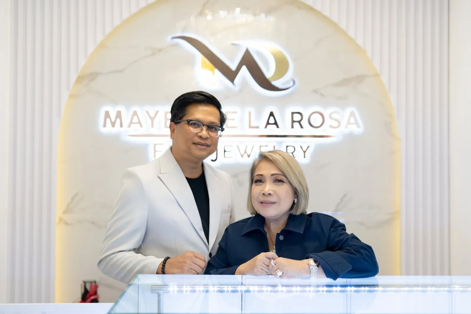 Richard and Mayet De La Rosa at the boutique counter, beneath the Mayet De La Rosa Fine Jewelry sign