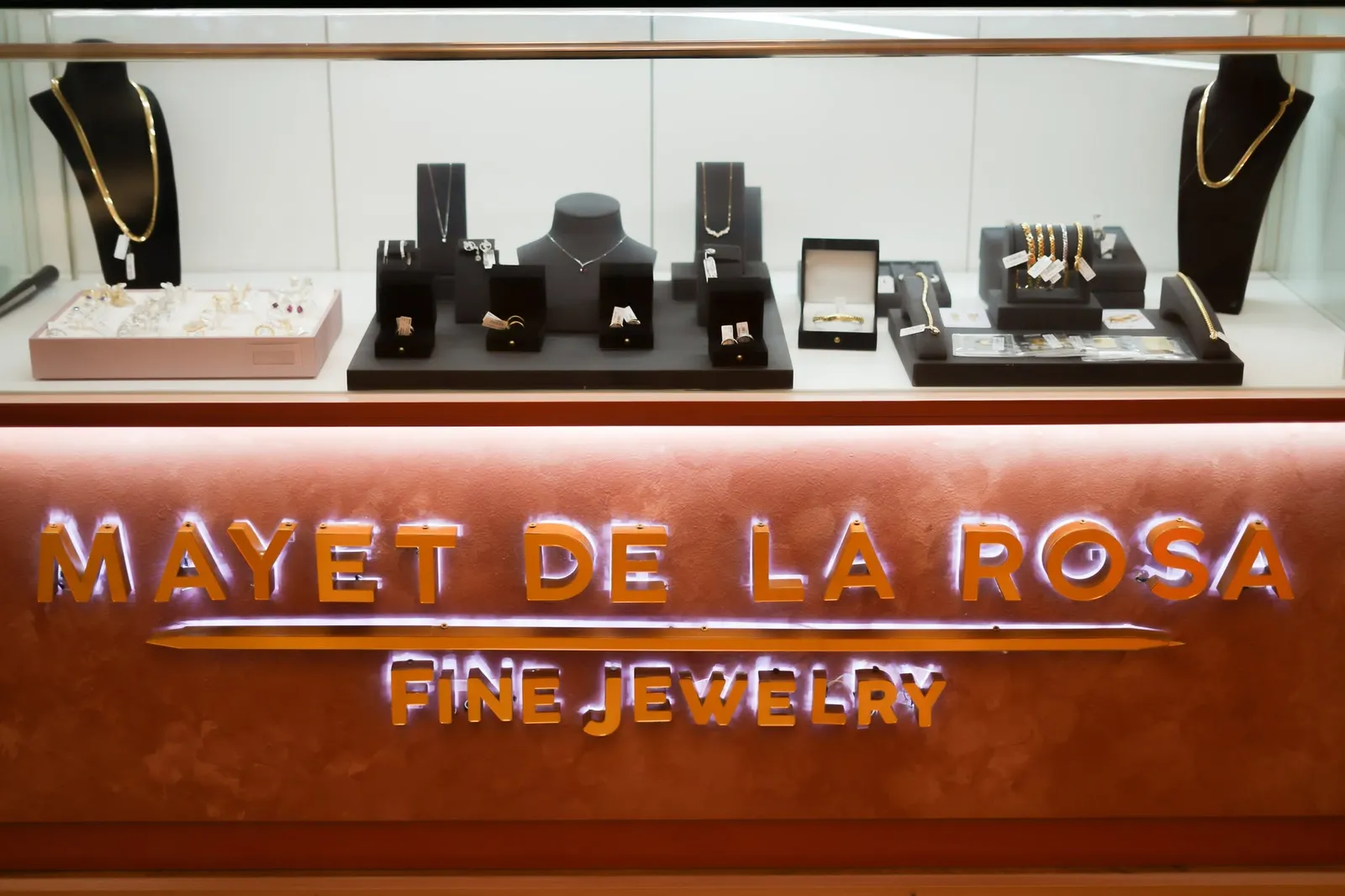 A lit Mayet De La Rosa Fine Jewelry showcase with necklaces, rings and bracelets on black stands